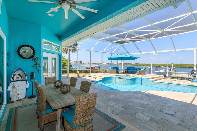 view of pool with glass enclosure, ceiling fan, a water view, and a patio