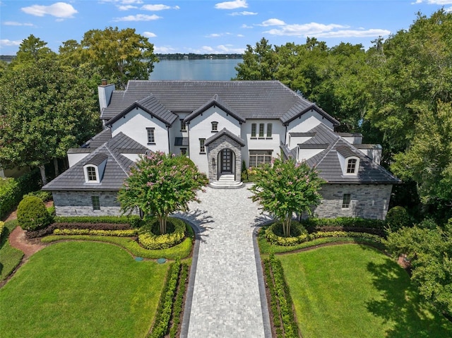 french provincial home with decorative driveway, stone siding, and a front yard