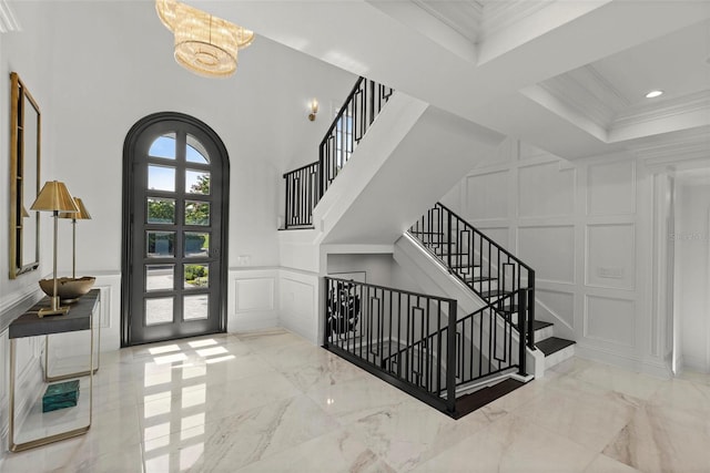 entryway with a notable chandelier, ornamental molding, a high ceiling, and french doors