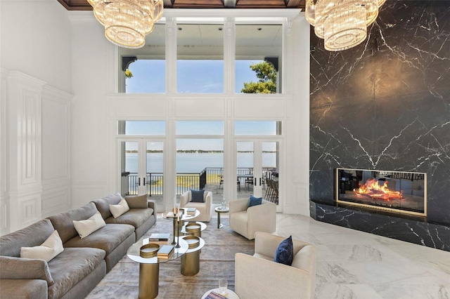 living room with french doors, a high ceiling, a premium fireplace, a notable chandelier, and a water view