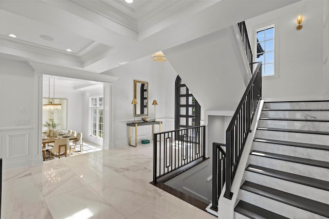 staircase featuring a wainscoted wall, a notable chandelier, marble finish floor, crown molding, and a decorative wall