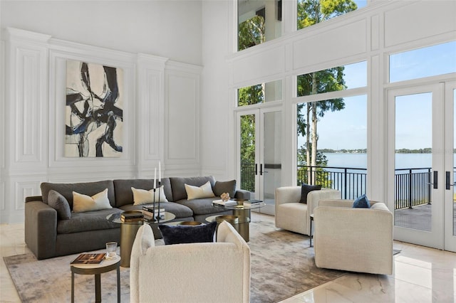 living area with french doors, a water view, a towering ceiling, and a decorative wall