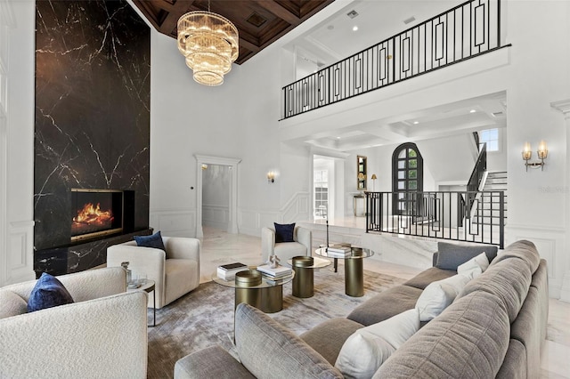 living area featuring stairway, coffered ceiling, a fireplace, a decorative wall, and a notable chandelier