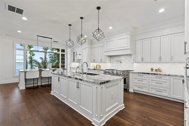 kitchen with dark hardwood / wood-style flooring, high end stainless steel range oven, a kitchen island with sink, sink, and white cabinets