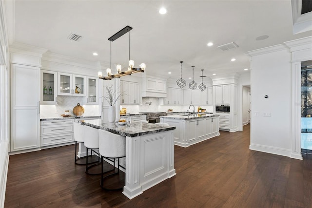 kitchen featuring visible vents, a center island with sink, crown molding, and stainless steel range