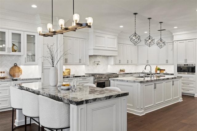 kitchen featuring light stone countertops, appliances with stainless steel finishes, dark hardwood / wood-style flooring, pendant lighting, and an island with sink