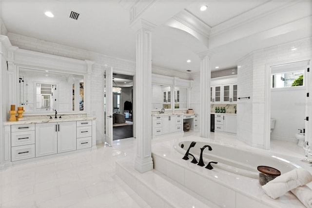 bathroom featuring decorative columns, a bathtub, vanity, tile walls, and ornamental molding