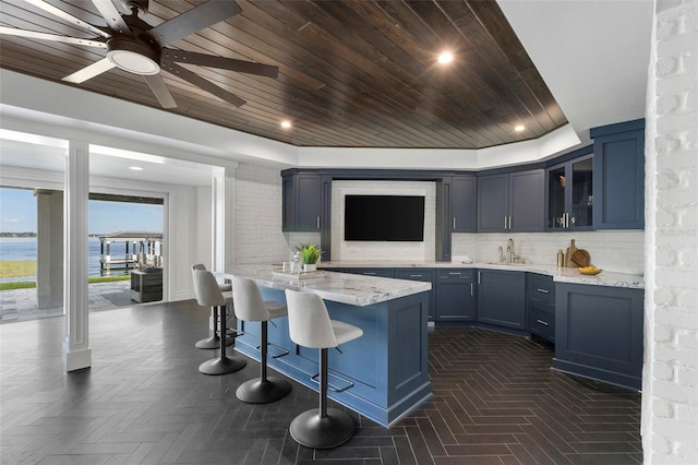 kitchen with a breakfast bar area, a sink, wood ceiling, glass insert cabinets, and backsplash