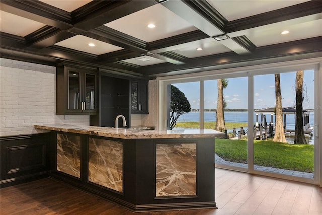 bar with coffered ceiling, a water view, light stone countertops, beamed ceiling, and wood-type flooring