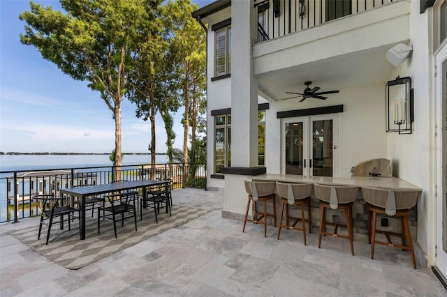 view of patio with outdoor dry bar, ceiling fan, a water view, french doors, and outdoor dining area