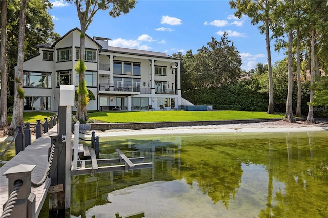 back of house featuring a water view, a balcony, and a lawn