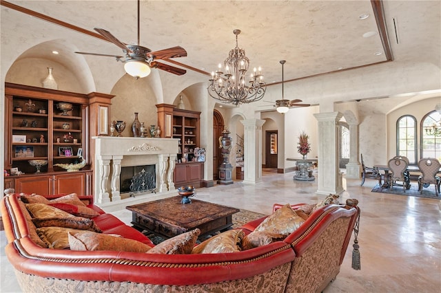 living room with decorative columns, a fireplace, ceiling fan with notable chandelier, and a high ceiling