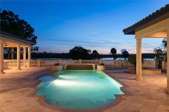 pool at dusk featuring a patio area and a water view