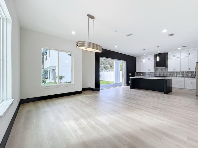 kitchen with a kitchen island, backsplash, pendant lighting, white cabinets, and light wood-type flooring