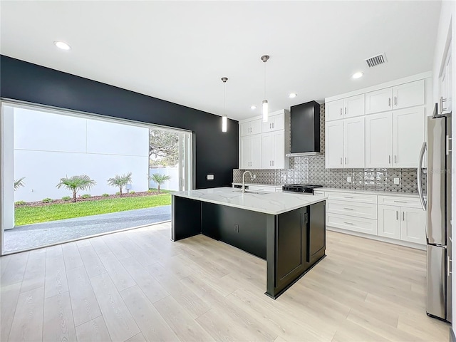 kitchen featuring white cabinetry, a center island with sink, wall chimney exhaust hood, and appliances with stainless steel finishes