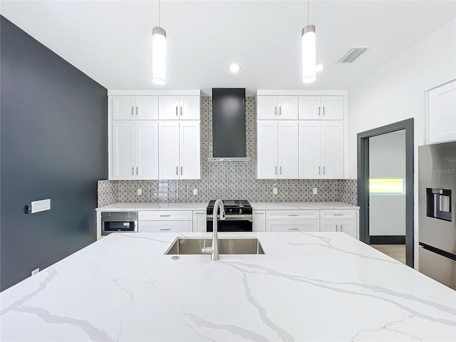 kitchen with appliances with stainless steel finishes, decorative light fixtures, white cabinetry, and wall chimney range hood