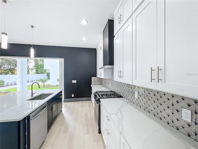 kitchen with light stone countertops, sink, hanging light fixtures, wall chimney range hood, and appliances with stainless steel finishes