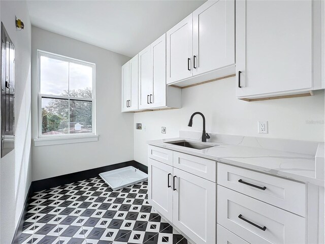 kitchen with light stone counters, white cabinetry, and sink