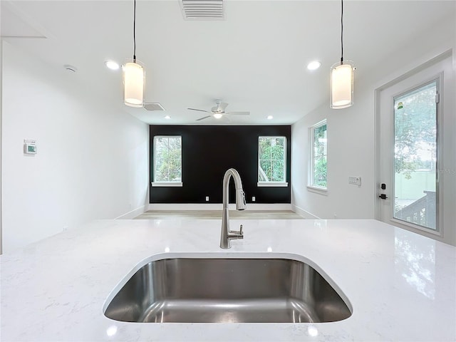 kitchen featuring light stone counters, sink, ceiling fan, and hanging light fixtures