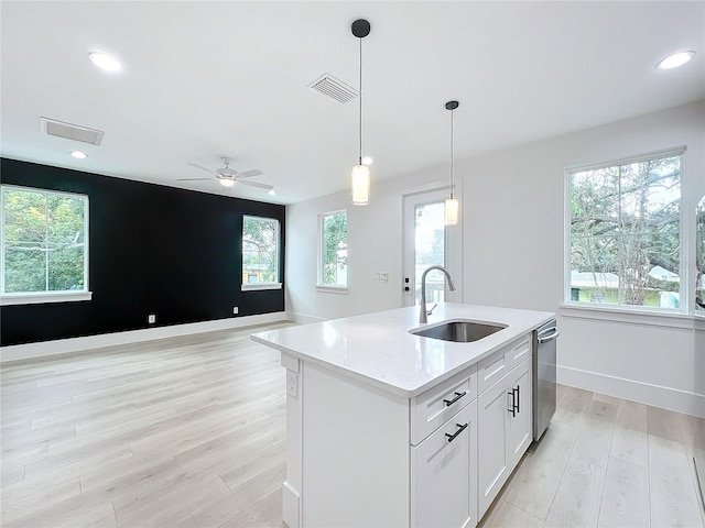 kitchen with stainless steel dishwasher, sink, decorative light fixtures, a center island with sink, and white cabinets