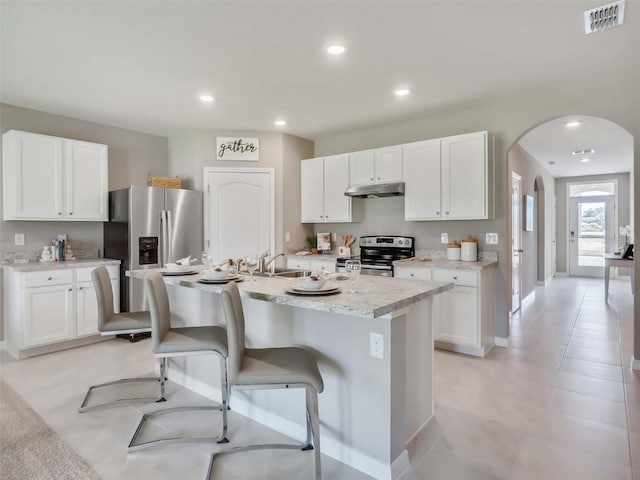 kitchen featuring white cabinets, a breakfast bar, stainless steel appliances, and a center island with sink