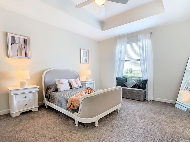 carpeted bedroom with a raised ceiling and ceiling fan