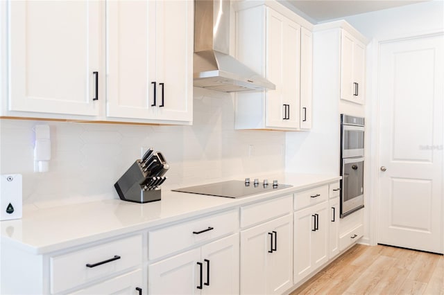 kitchen featuring light hardwood / wood-style flooring, wall chimney exhaust hood, tasteful backsplash, white cabinetry, and stainless steel double oven