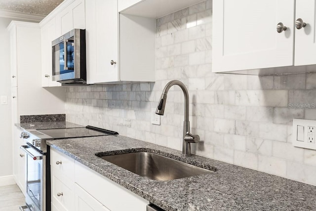 kitchen featuring tasteful backsplash, dark stone counters, stainless steel appliances, sink, and white cabinets