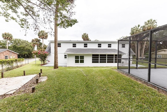 rear view of house with glass enclosure and a yard