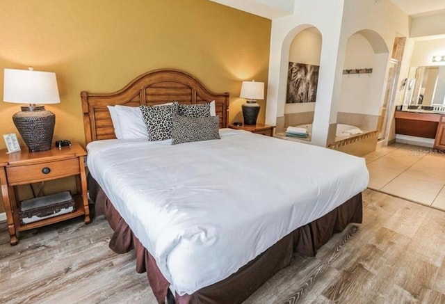 bedroom featuring ensuite bath, light wood-style flooring, and arched walkways