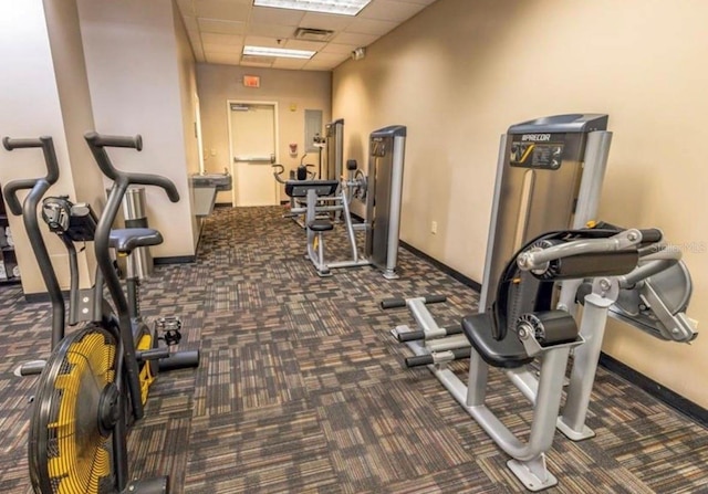 exercise room featuring visible vents, a paneled ceiling, and baseboards