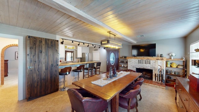 dining room with track lighting, wood ceiling, beam ceiling, light tile patterned floors, and a fireplace