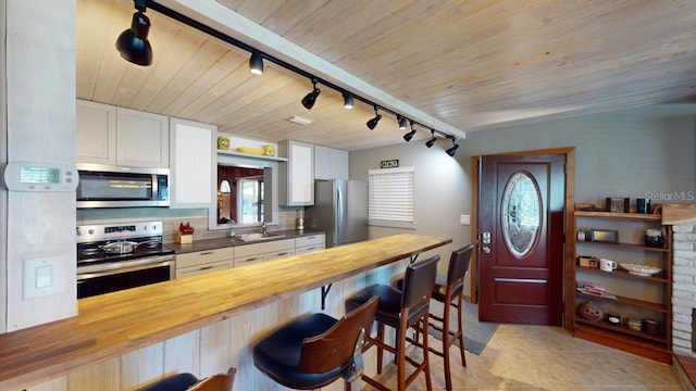 kitchen with track lighting, white cabinets, a kitchen breakfast bar, appliances with stainless steel finishes, and butcher block countertops