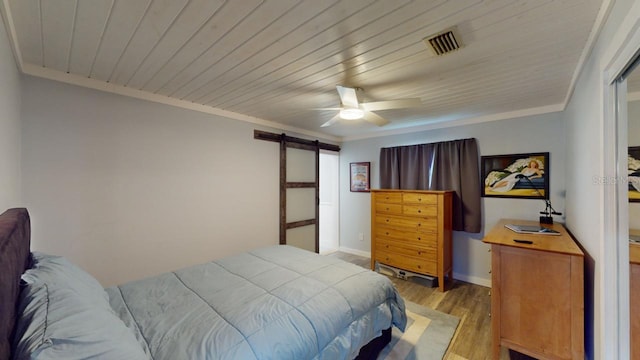 bedroom featuring light wood-type flooring, a barn door, ceiling fan, and ornamental molding