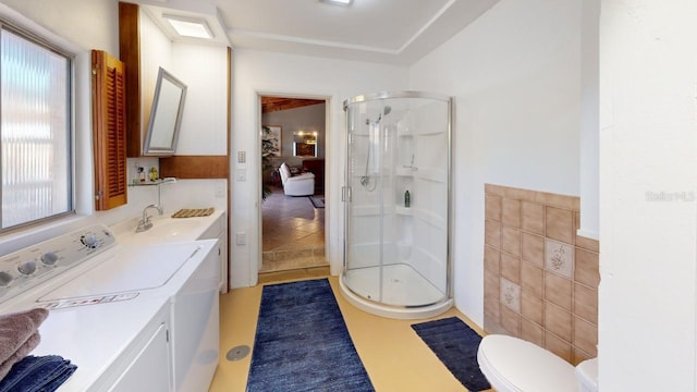 bathroom with vanity, toilet, washing machine and dryer, tile walls, and a shower with shower door