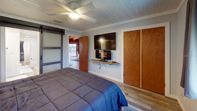 unfurnished bedroom with ornamental molding, ceiling fan, a barn door, hardwood / wood-style flooring, and a closet