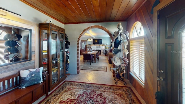 foyer entrance featuring a stone fireplace, wood walls, light tile patterned flooring, wood ceiling, and ornamental molding