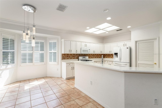 kitchen with pendant lighting, decorative backsplash, white appliances, white cabinetry, and a skylight