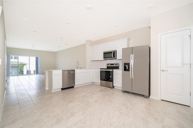 kitchen featuring white cabinets, appliances with stainless steel finishes, a peninsula, a sink, and backsplash