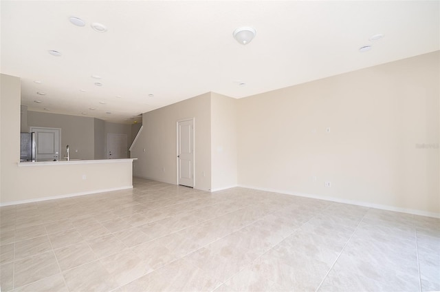 empty room featuring light tile patterned floors, stairway, a sink, and baseboards