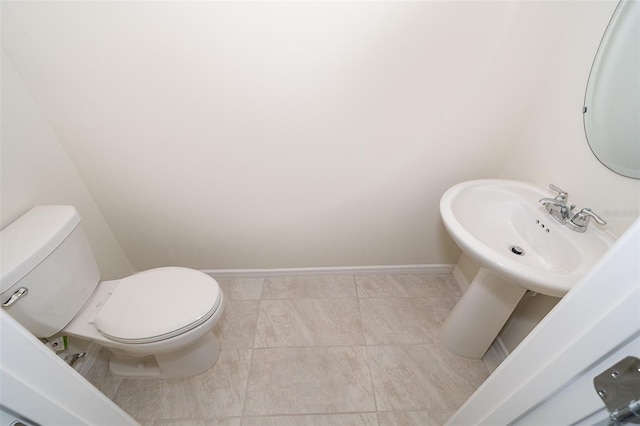 half bathroom with toilet, baseboards, a sink, and tile patterned floors