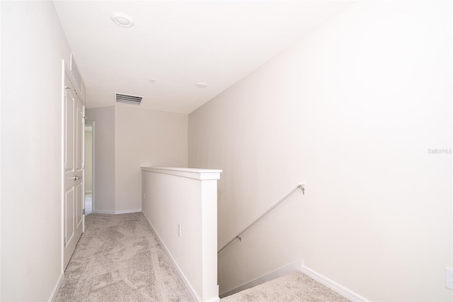 hallway featuring carpet floors, baseboards, visible vents, and an upstairs landing