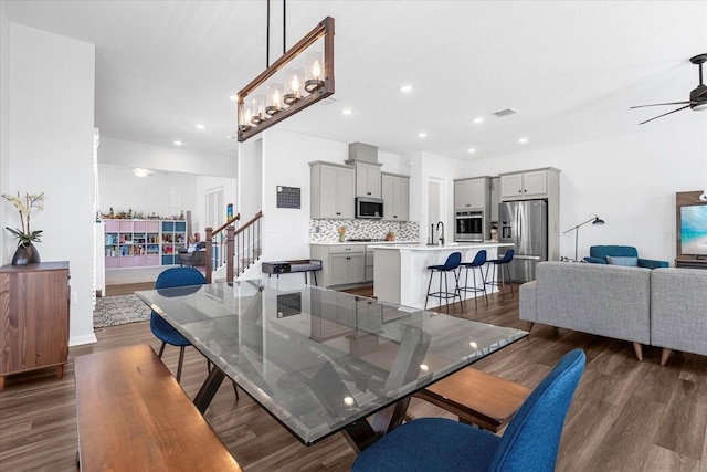 dining room with sink, dark wood-type flooring, and ceiling fan with notable chandelier