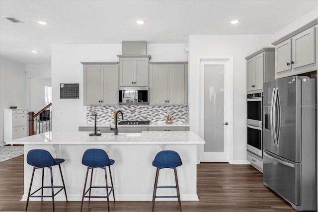 kitchen featuring gray cabinets, a center island with sink, stainless steel appliances, and dark hardwood / wood-style floors