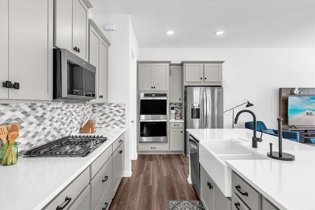 kitchen with dark wood-type flooring, sink, decorative backsplash, gray cabinets, and stainless steel appliances