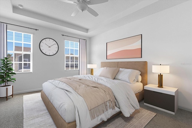 carpeted bedroom with a tray ceiling, multiple windows, and ceiling fan