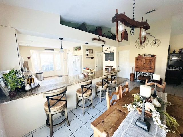 kitchen featuring light tile patterned flooring, a peninsula, a breakfast bar area, and freestanding refrigerator