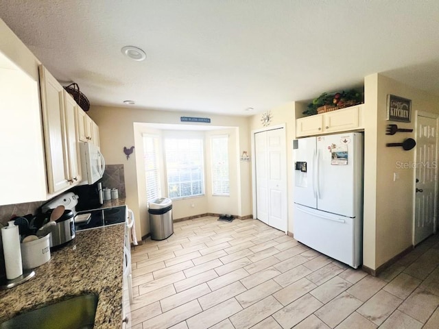 kitchen with baseboards, dark stone countertops, white appliances, white cabinetry, and a sink