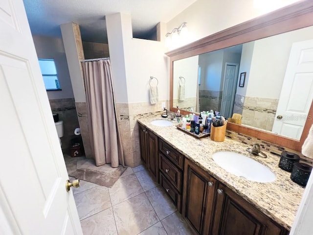 full bath with tile walls, double vanity, a wainscoted wall, and a sink