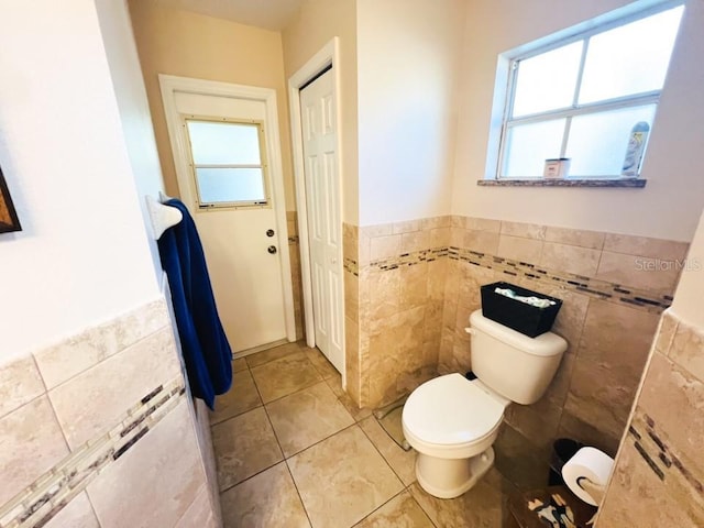 bathroom with a wealth of natural light, toilet, tile walls, and tile patterned floors